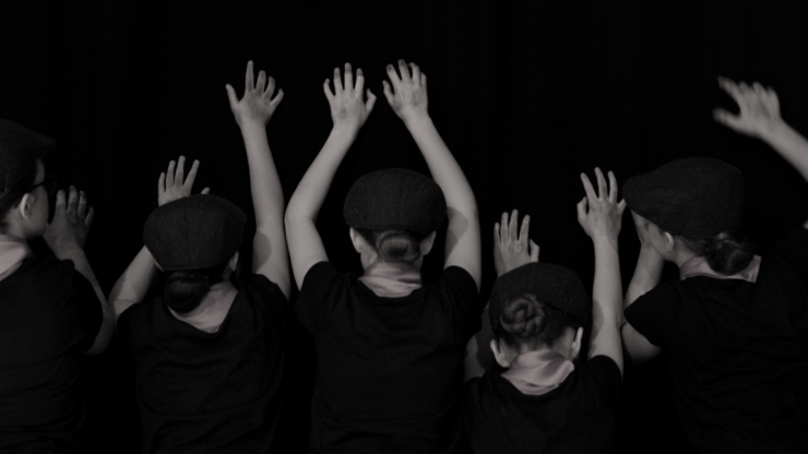 Children in black t-shirts, with their backs to the camera and their arms in the air.